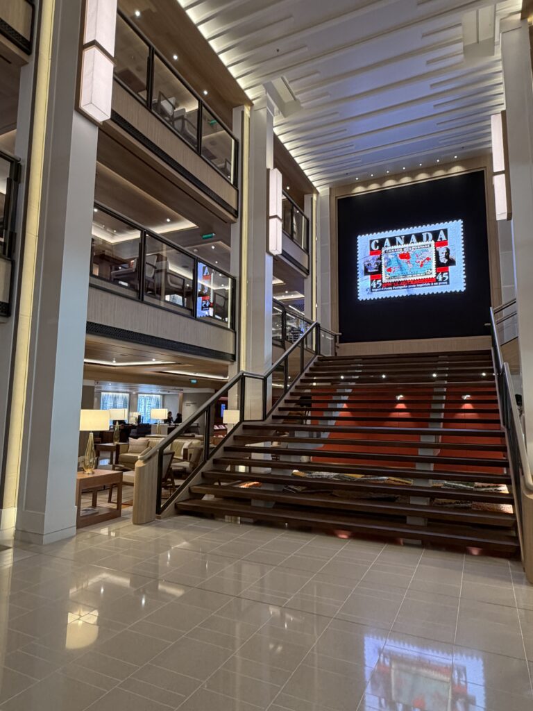 Viking Mars atrium with a broad staircase, wood finishes and a large screen displaying a Canadian postage stamp.