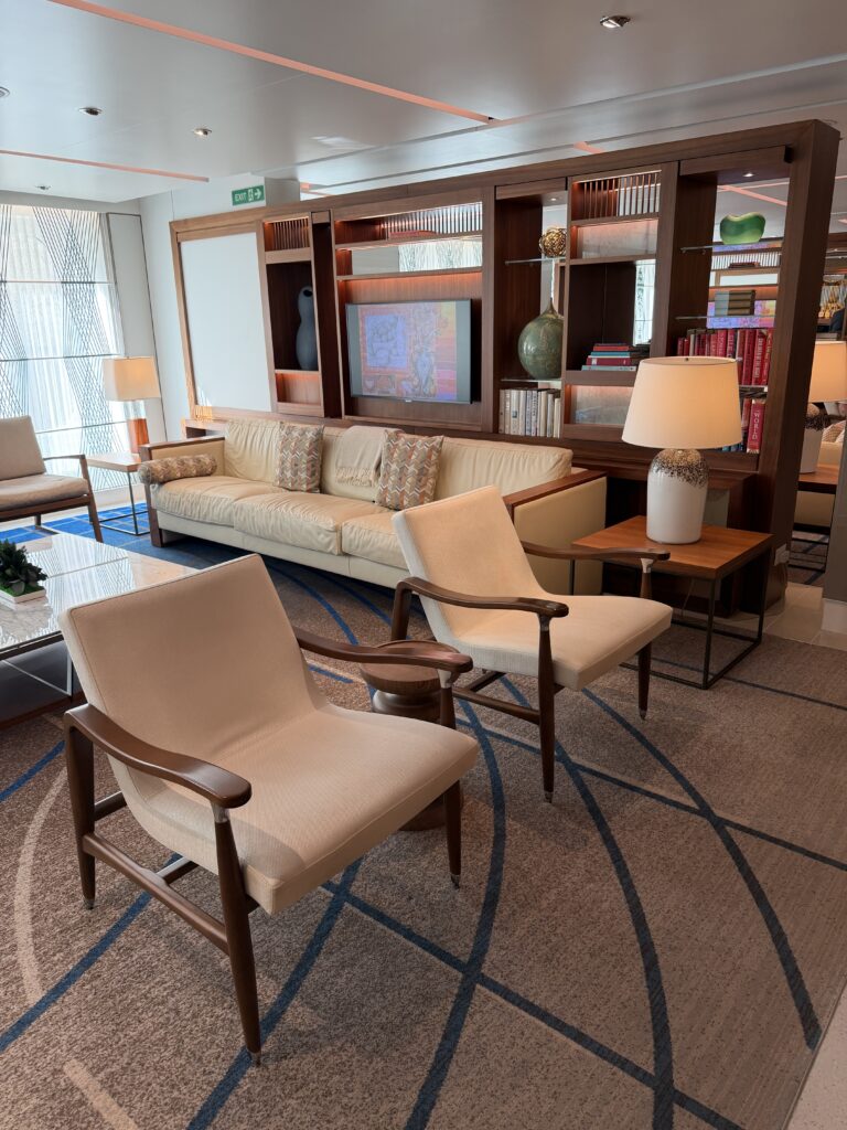 Cream sofa and armchairs in The Living Room aboard Viking Mars, surrounded by books, artwork and wood shelving.
