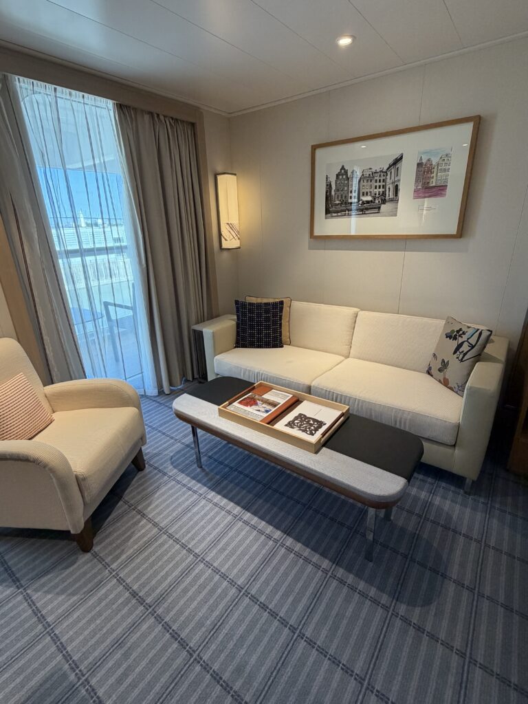 Viking Mars stateroom sitting area with a cream sofa, armchair, coffee table and glass doors leading to the veranda.